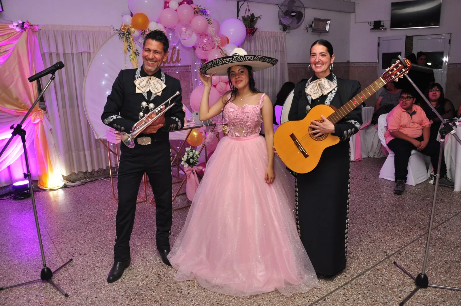 La quinceañera, con vestido rosa y sombrero de mariachi, junto al dúo Experiencia Guadalupe en su fiesta de 15