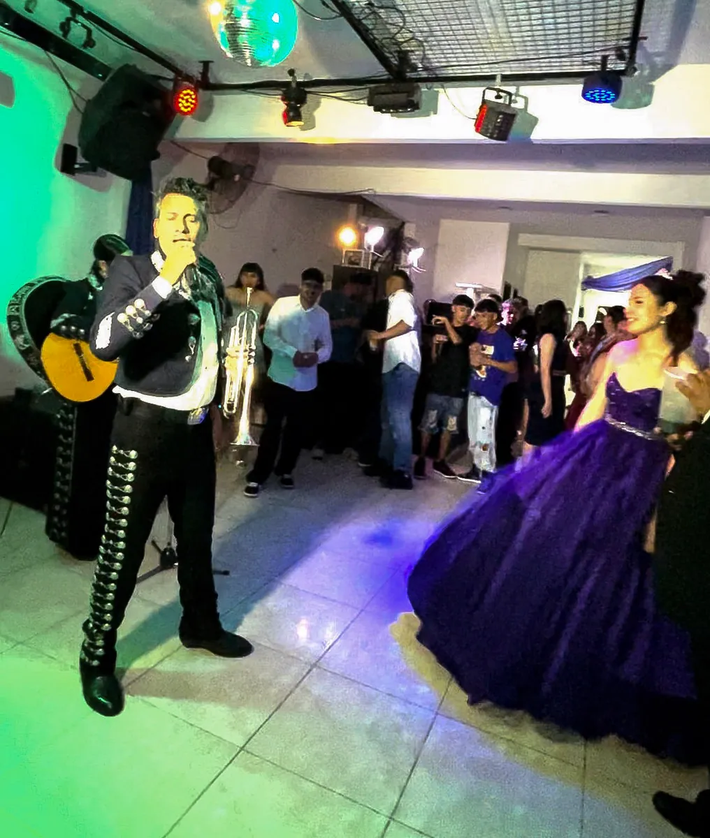 El guitarrista de Experiencia Guadalupe toca en la pista mientras la quinceañera, de vestido violeta, baila con sus invitados