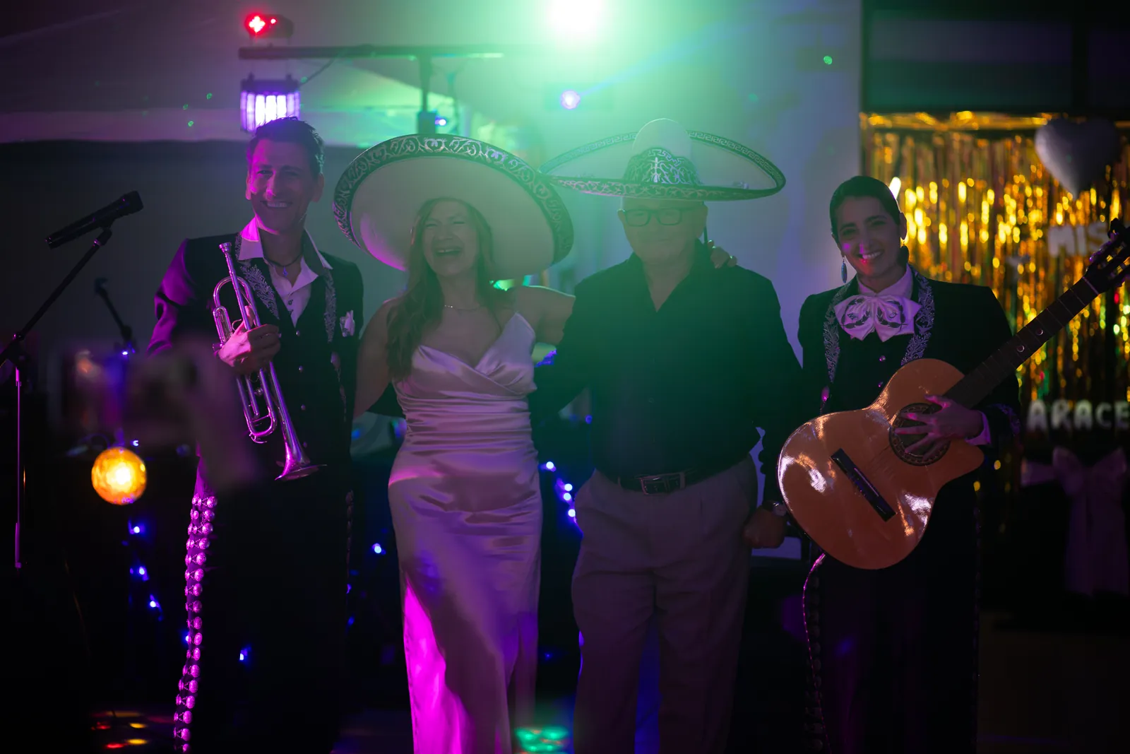 Una pareja festeja entre los mariachis, con trompeta y guitarra, bajo luces de colores