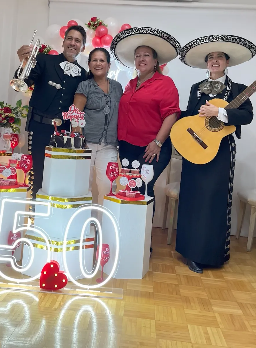 Festejo de 50 años: dos invitadas posan con los mariachis junto al número 50 iluminado