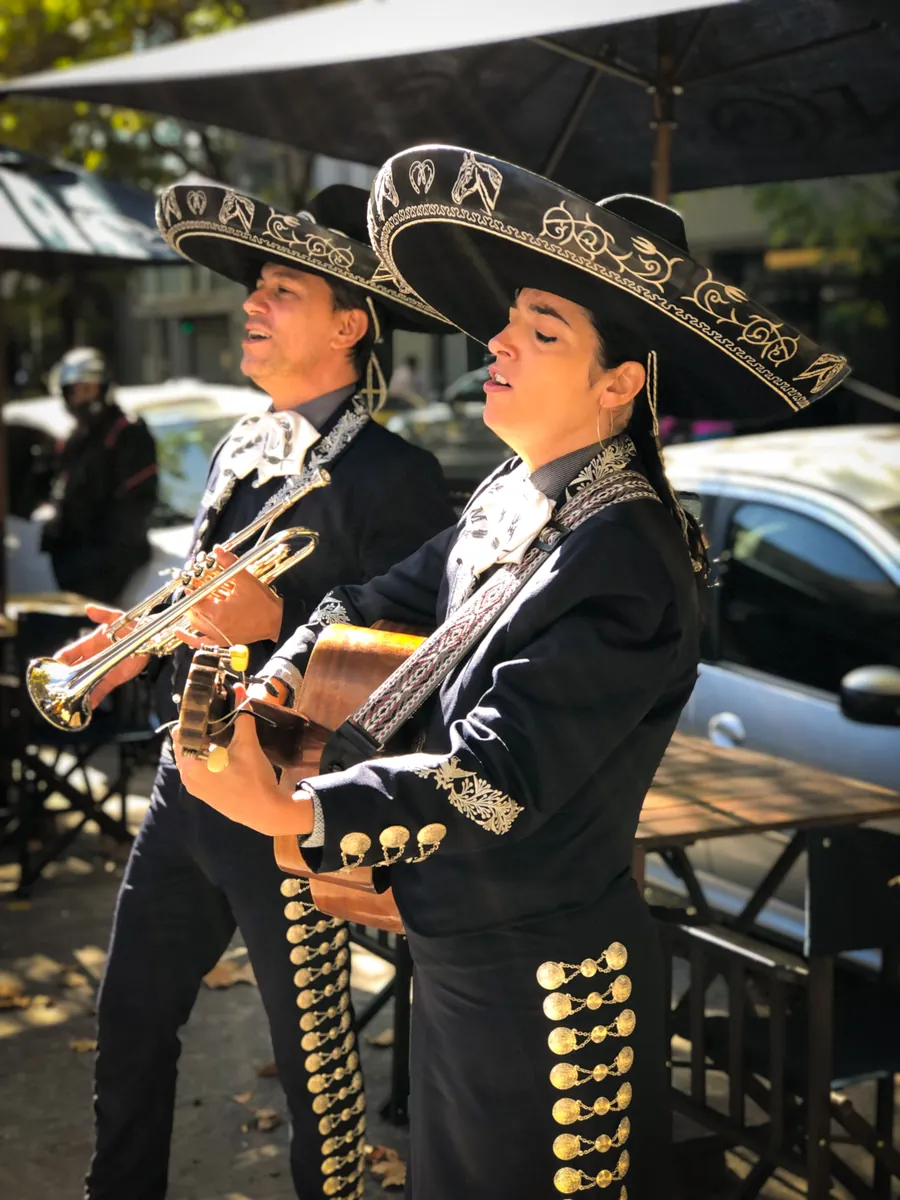 Dos mariachis de Experiencia Guadalupe tocan trompeta y guitarra en la vereda
